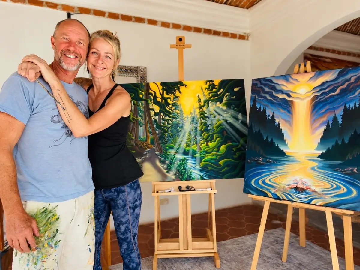 Grant Pecoff and Stephanie Clair smiling together in their studio with two Gemini paintings