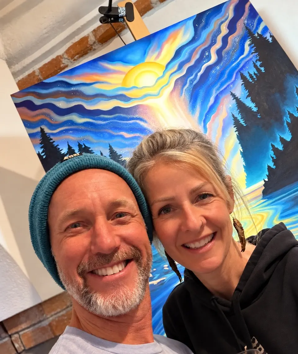 Grant Pecoff and Stephanie Clair smiling together in their studio in front of a Gemini painting